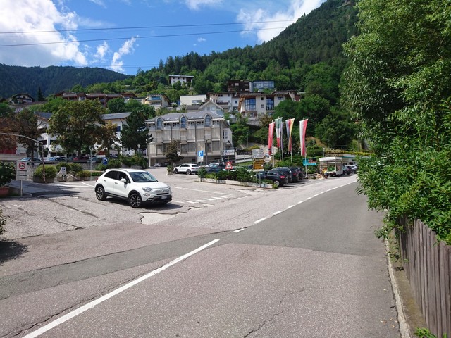 Mühlbach: Zwischen den zwei abgestellten weißen Autos sieht man die Straße, die hier startet, und nach Spinges hinauf führt.