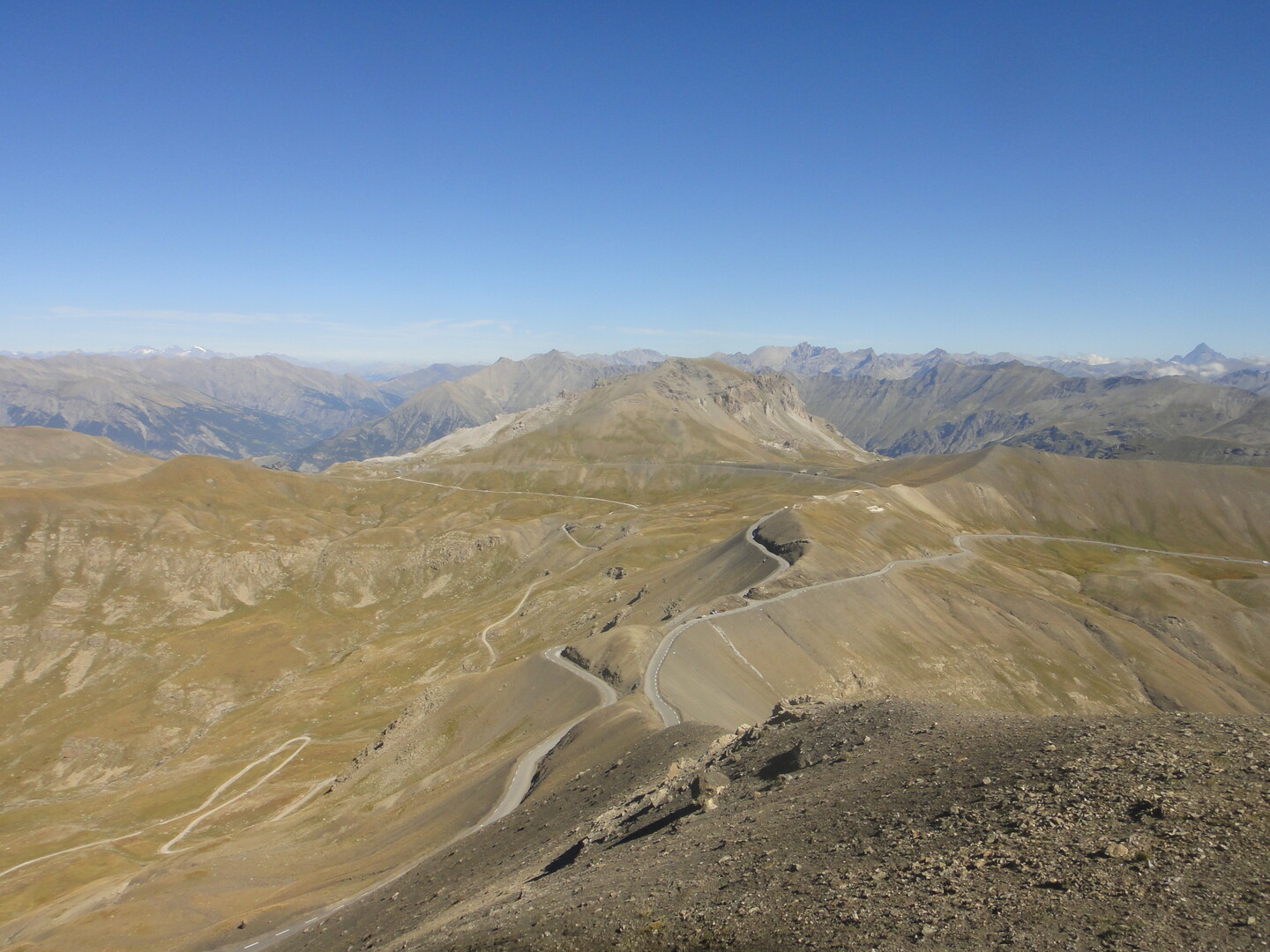 Blick vom Gipfel der Cime de la Bonette (2680 m) auf die Passhöhe, den Col de la Bonette. Der Berg, der sich im Mittelgrund erhebt, ist der Sommet de Restefond. Links davon liegt der Faux Col de Restefond, rechts unterhalb der Col de Restefond. Die nördliche Passstraße aus Richtung Jausier quert den ersten und touchiert den zweiten, jeweils ansteigend.
Hinten links sieht man die Barre des Écrins, den südlichsten und westlichsten 4000er der Alpen.
Ganz hinten rechts ragt der dreiecksförmige Monviso (3841 m) hervor, der höchste Gipfel der Cottischen Alpen. 