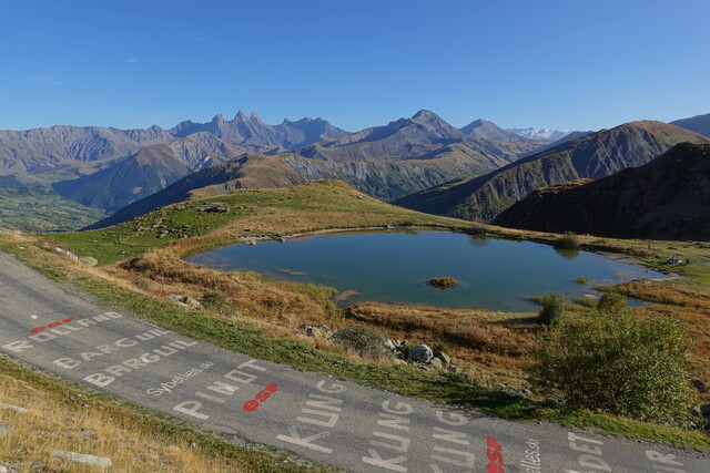 Schöner geht's kaum: schmale Straße ohne Verkehr, die Aiguilles d'Arves und der Meije-Gletscher (eigentlich: Glacier de la Girose) im Hintergrund, mit Bergsee und Vallée de l'Arvan.