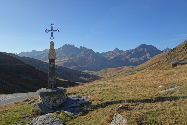 Die Passhöhe mit dem Croix de Fer, dem eisernen Kreuz. Im Hintergrund, klein und unscheinbar, die Passhöhe des Glandon und die Schussgerade der Südrampe durch die Wiesenlandschaft.
